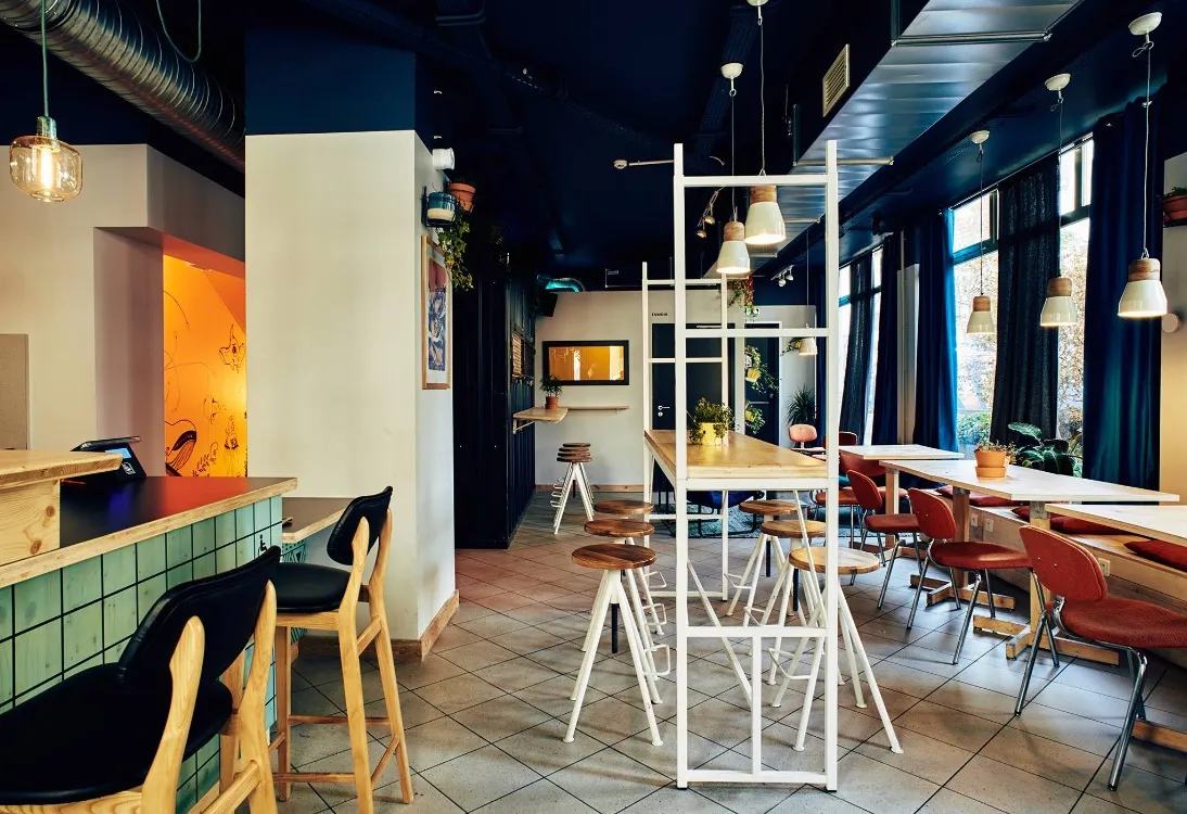 La salle du bar : comptoir carrelé, tables hautes et grandes baies