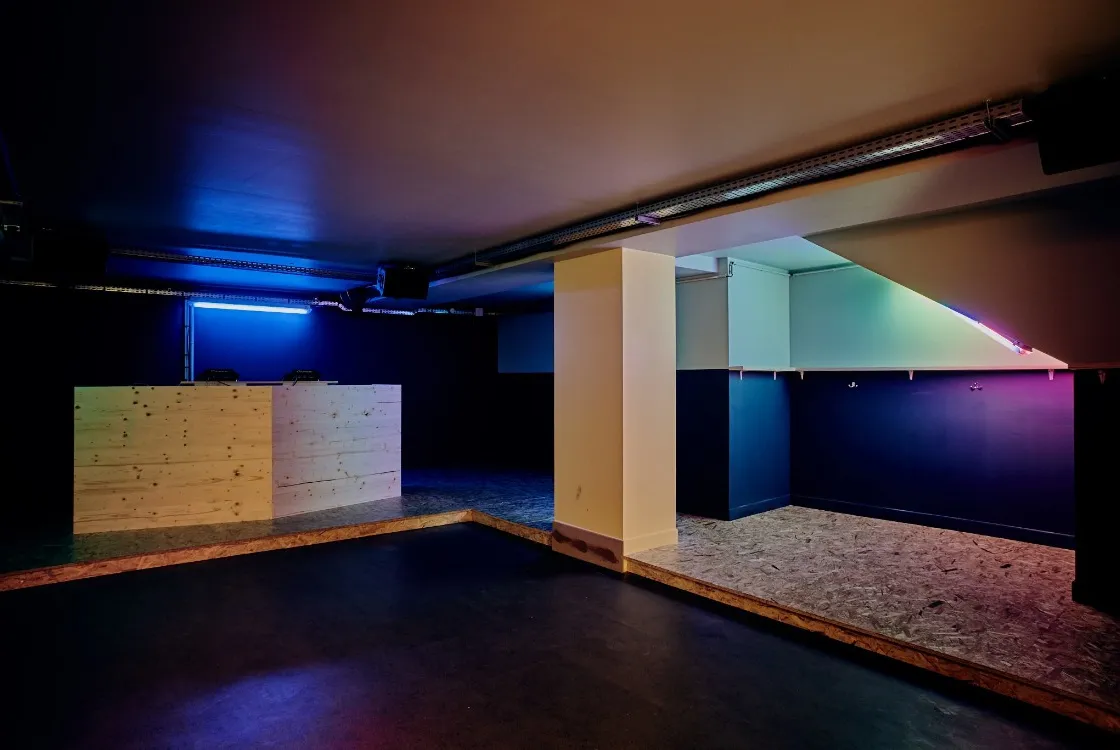 Le club au sous-sol : cabine DJ en bois, néons bleus et roses